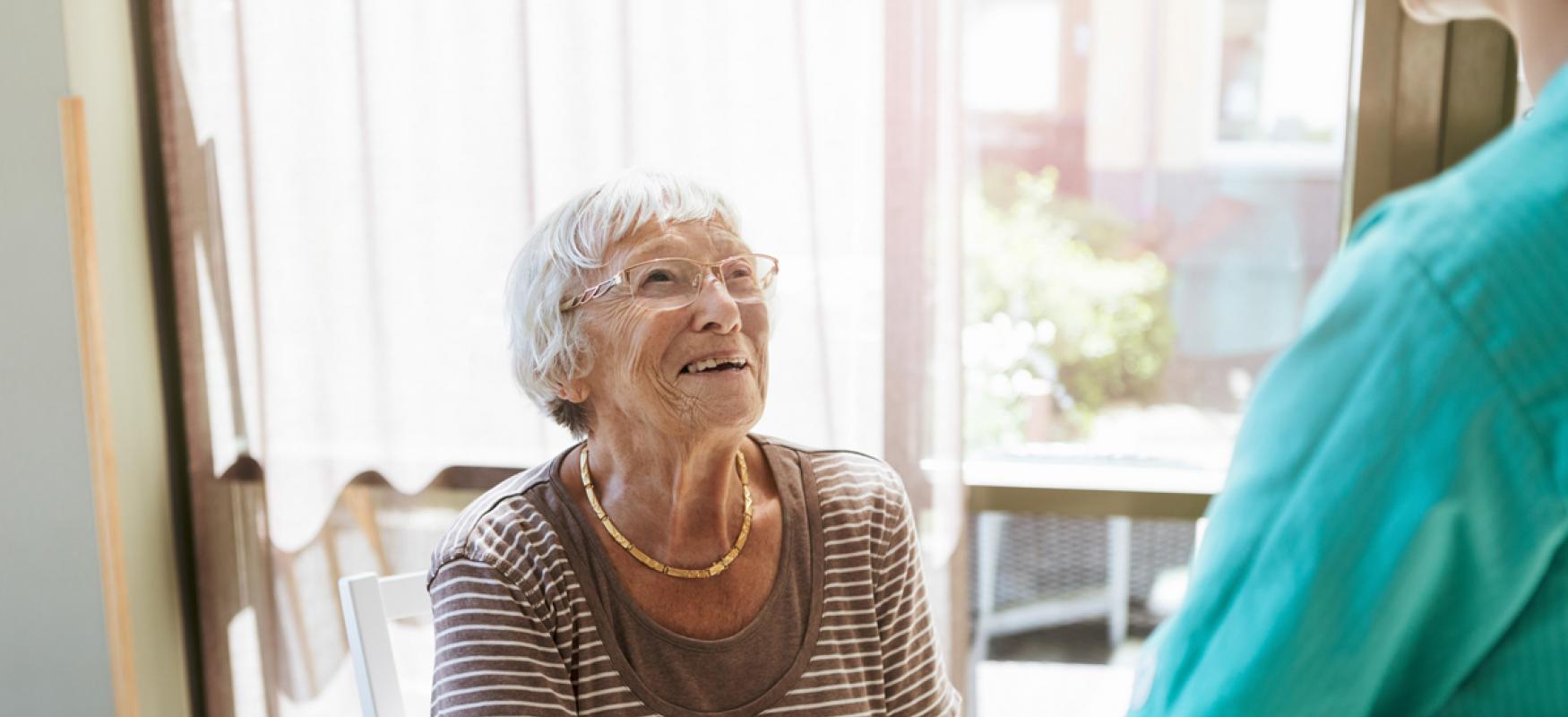 Elderly woman on a chair holding the hands of a nurse.